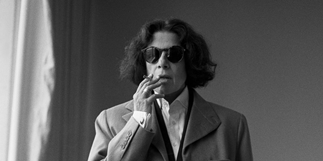 Woman in blazer and sunglasses smoke in black and white.