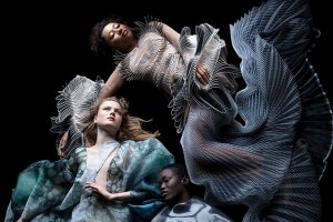 Three models float in black space wearing sculptural gowns.